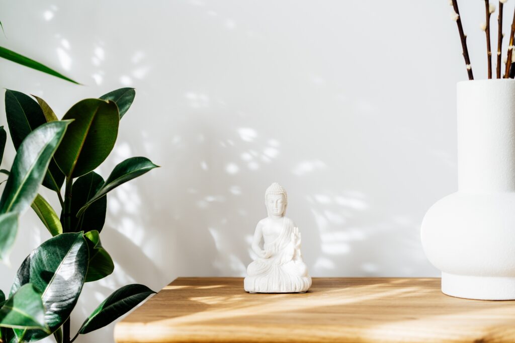 White Buddha statuette home decoration and clay vase standing on wooden cabinet. Minimalist design